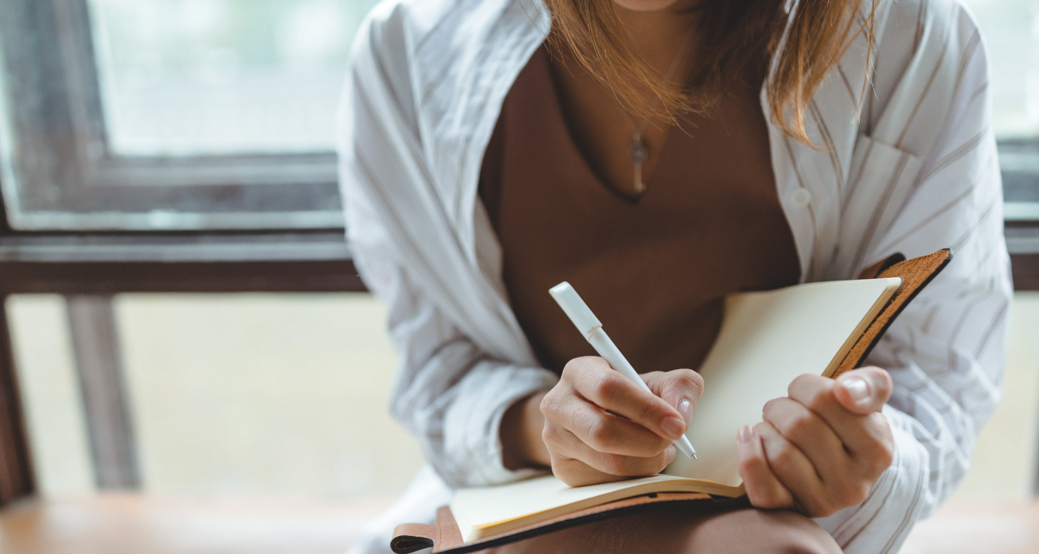 Woman in front of window writing in an open journal